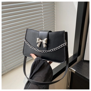 Close-up of matte black underarm bag with silver metal bow and decorative chain link