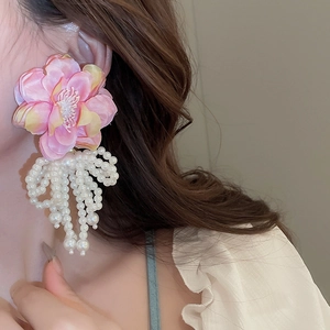Detailed close-up of pink and yellow mesh flower earrings with white pearl tassels on model