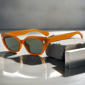 Close-up of amber cat-eye sunglasses with green lenses on stone and metal props