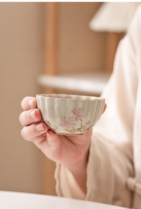 Detail of hand-held ceramic teacup with daisy floral patterns and scalloped rim edge
