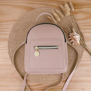 Pink PU leather mini backpack for women on woven mat with professional wooden background