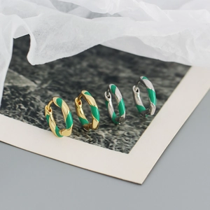 Macro shot of gold and silver spiral enamel huggie earrings on white textured paper
