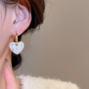 Close-up of white heart drop earrings with gold metal hoop on a female model