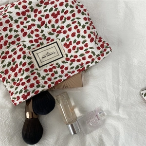 Detailed shot of white pleated cherry print makeup bag with cosmetics on a soft cloth