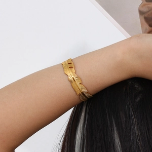 Close-up of golden feather leaf bracelet on wrist showing detailed metal texture