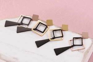 Close-up of geometric titanium steel earrings in gold and black on a textured surface