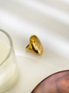 Close-up of a chunky oval gold ring with a polished mirror finish on a minimalist surface