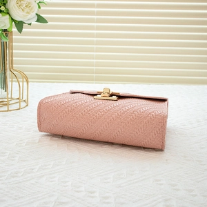 Pink woven leather crossbody handbag with gold clasp on white lace tabletop