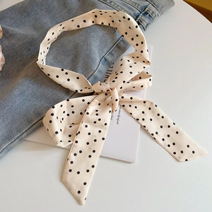 Detail of light beige silk scarf with black polka dot pattern tied in a bow