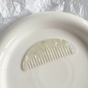 Close-up of white acetate half-moon pocket hair comb on minimalist ceramic plate