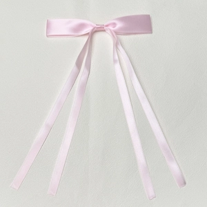 Detail of pink satin ribbon bow hair clip with four long streamers on leather background