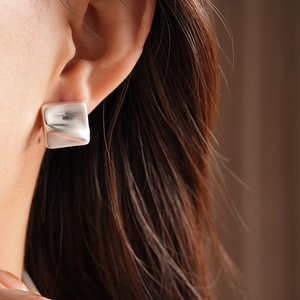 Macro shot of silver square earrings with unique folded texture on a female model