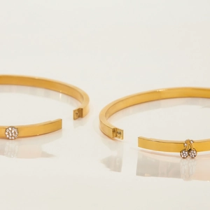 Dettaglio di bracciali in acciaio dorato 18K con motivi a cerchio e ciliegia in cristallo