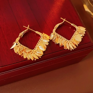 Detailed view of gold plated square hoop earrings with textured leaf tassels on a jewelry box