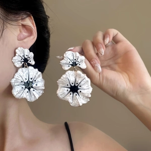 Macro detail of large white flower earrings with black accents and center pearl on model