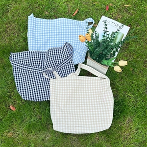 Three checkered canvas tote bags in blue, black, and beige colors on green grass