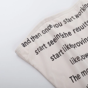 Makroaufnahme des cremefarbenen Tube-Tops mit schwarzem Buchstaben-Aufdruck und Mesh-Gewebe