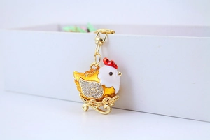 Detailed view of a golden hen keychain with rhinestones and enamel on a white box edge