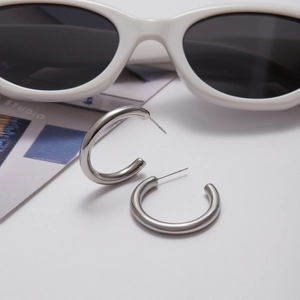 Polished silver C-shape hoop earrings styled with fashion sunglasses and a magazine