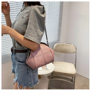 Pink PU leather shell chain bag worn by model in a bright minimalist indoor setting