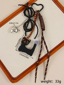 Detail of cute black cat plush keychain with silver heart charm and braided strap