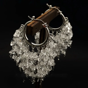 Close-up of elegant silver crystal tassel earrings hanging on a wooden display stand