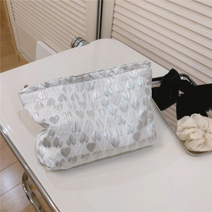 Detail of white satin cosmetic bag with elegant silver heart jacquard texture and zipper