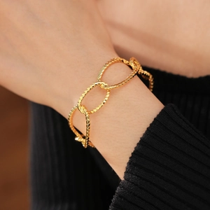 Close-up of gold-plated irregular oval link bracelet on a wrist with black knit cuff