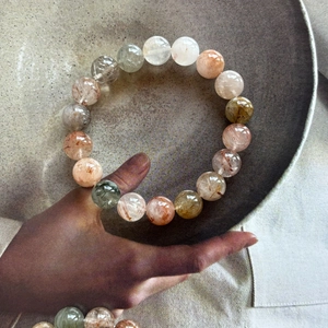 Detailed view of polished natural multi-color rutilated quartz beads on a minimalist artistic base