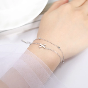 Detail of silver double-layer stainless steel bracelet featuring an X-shaped pendant