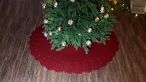 Detail of dark red knitted Christmas tree skirt with hollowed wave edges on wood floor