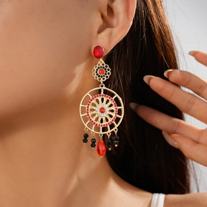 Close-up of golden bohemian dreamcatcher drop earrings with red gems and sparkling rhinestones