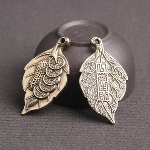 Detail of two vintage brass leaf pendants with Chinese prosperity symbols on a pottery jar