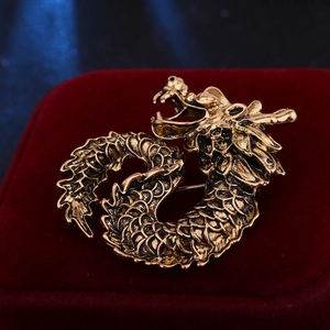 Close-up of vintage bronze dragon brooch on red velvet background with antique texture