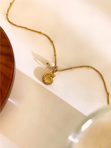 Detailed close-up of a gold conch pendant necklace with a single freshwater pearl accent