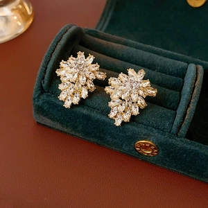 Macro shot of gold-plated leaf earrings with cubic zirconia in green velvet box