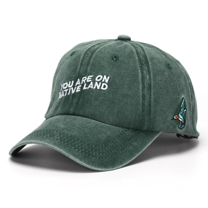 Detail of white embroidery text and colorful bird on dark green washed cotton baseball cap