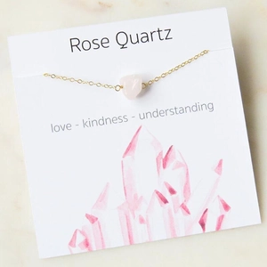 Detailed close-up of rose quartz stone on gold chain with card featuring love and kindness