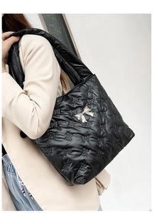 Quilted black tote bag with 3D bow texture and silver metallic bow charm on model