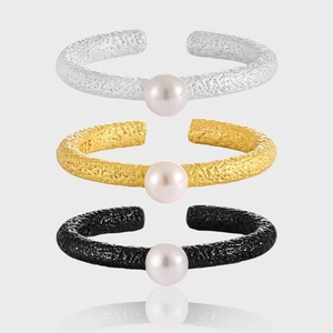 Three textured open rings with pearls in silver, gold, and black finishes stacked vertically