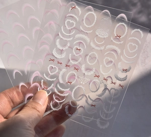Detailed view of lace and red bow nail stickers with transparent backing on hand