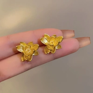 Detailed close-up of golden 3D flower stud earrings with matte metallic texture and petals