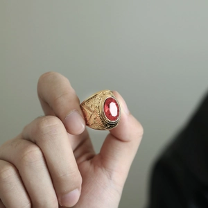 Detalle del anillo dorado vintage con gema roja y grabado del Ojo de la Providencia