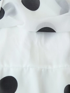 Nahaufnahme von weißem Chiffonstoff mit schwarzen Punkten zeigt Textur und feine Nähte