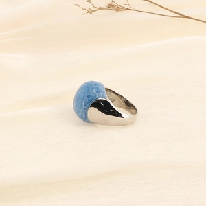 Close-up of light blue enamel ring with silver band on minimalist beige fabric background