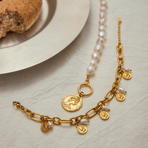 Detailed shot of gold coin pendant bracelets with baroque pearls on linen background