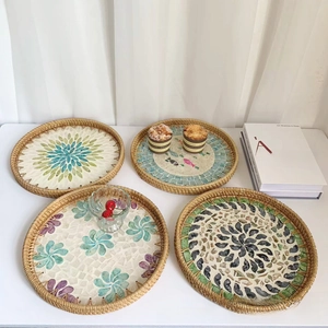 Detail of four handmade rattan trays with shell mosaic patterns on a white table