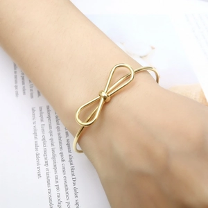 Detailed view of an elegant gold bow-knot open bangle bracelet on a woman's wrist