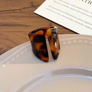 Detailed close-up of a wide tortoiseshell acrylic ring on a minimalist ceramic plate