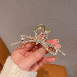 Détail d'une pince à cheveux en métal doré avec strass et une perle en forme de nœud